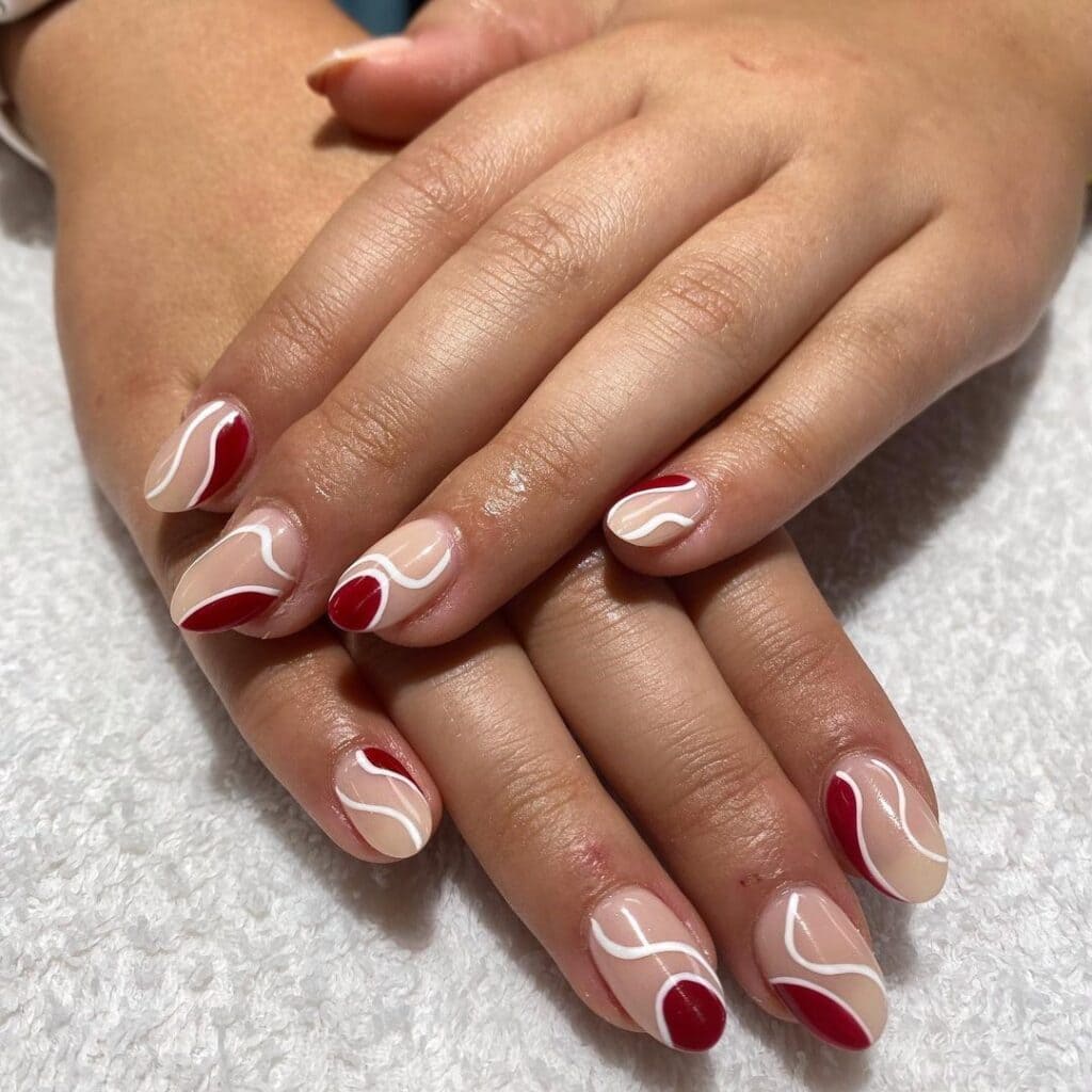 A hand displaying burgundy and white swirl nail art x