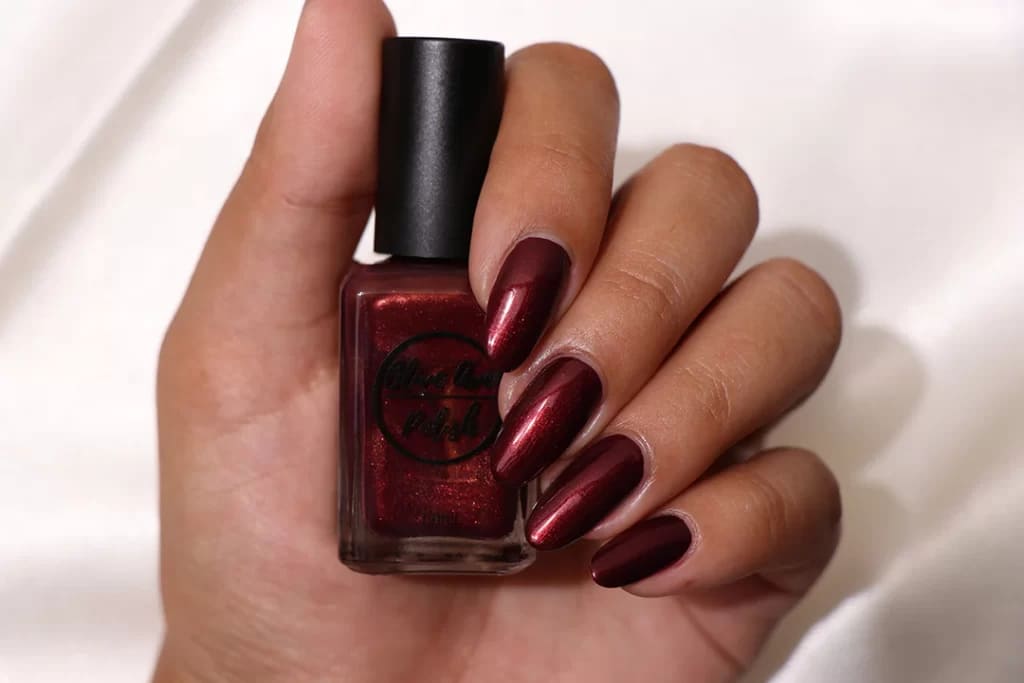 A hand holding a burgundy nail color showing off burgundy metallic nail color x