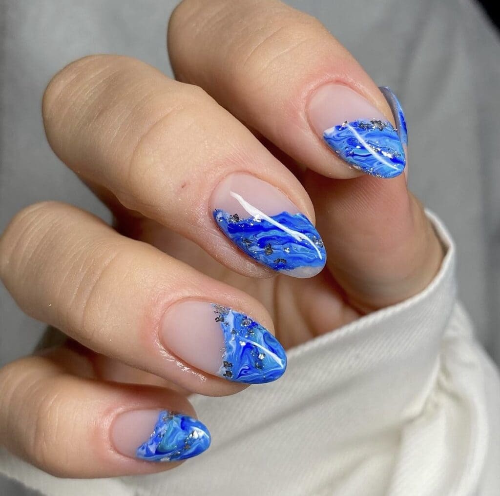 A hand showing off blue ocean art glittery manicure x