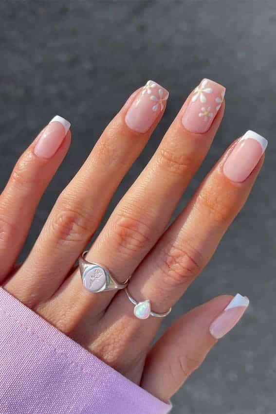A hand with rings displaying square nails and french white tips with flowers