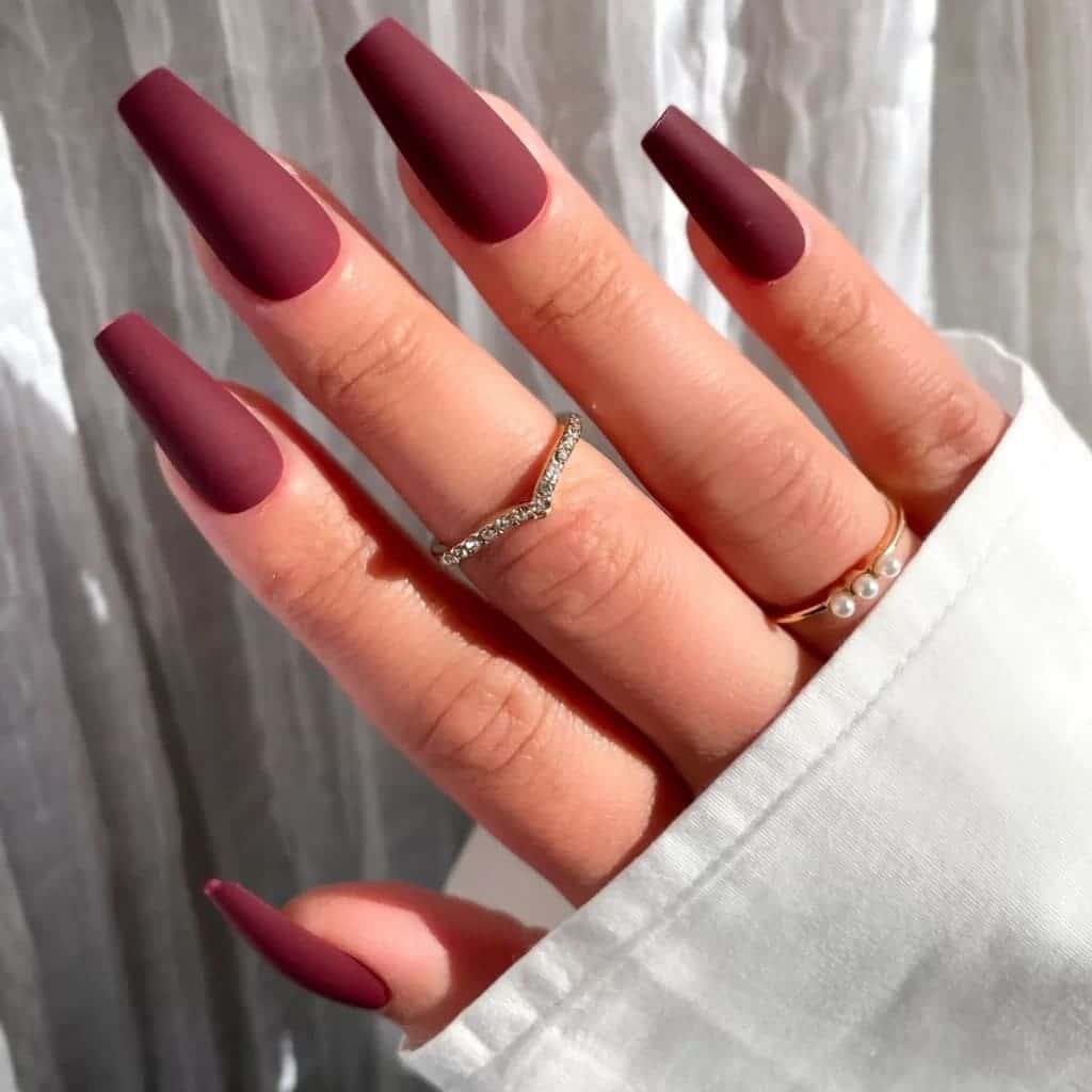 A hand with rings showing matte burgundy long coffin nails x