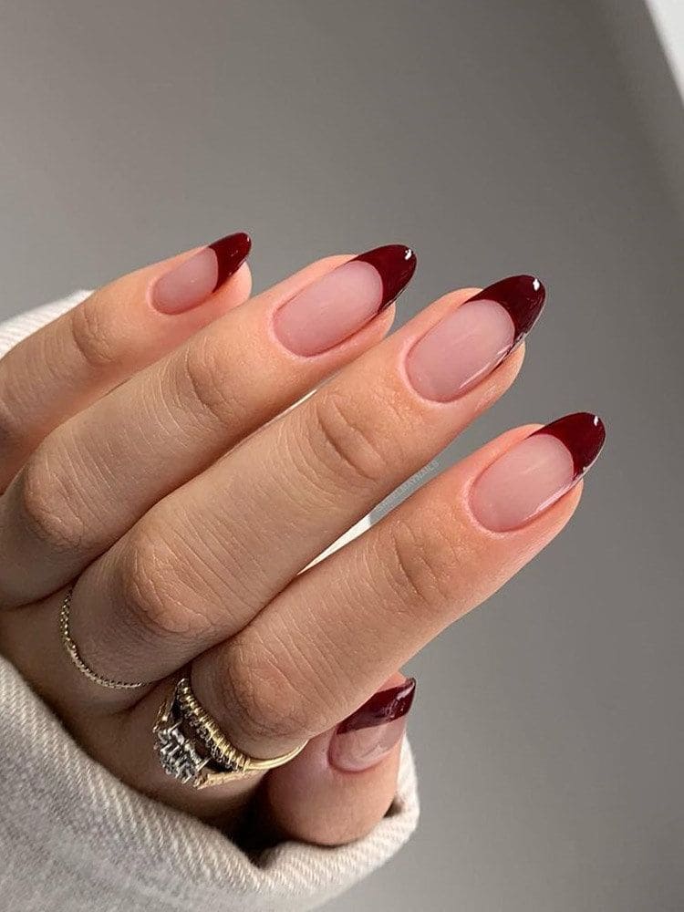 A hand with rings showing off maroon painted nail tips