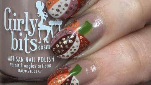 A view of a hand holding a brown nail polish with pumpkin design nail art