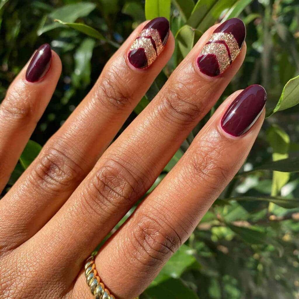 A view of hands displaying burgundy nails with arrow shaped golden glittery foil accent x