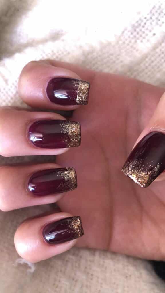 A view of nails with burgundy nail color and a dash of gold glitter on the tips x