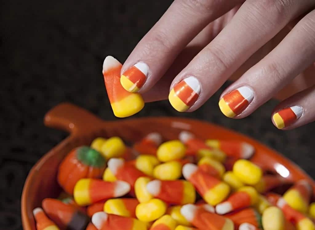 A view of white orange and yellow candy corn nailk design on hand holding a candy