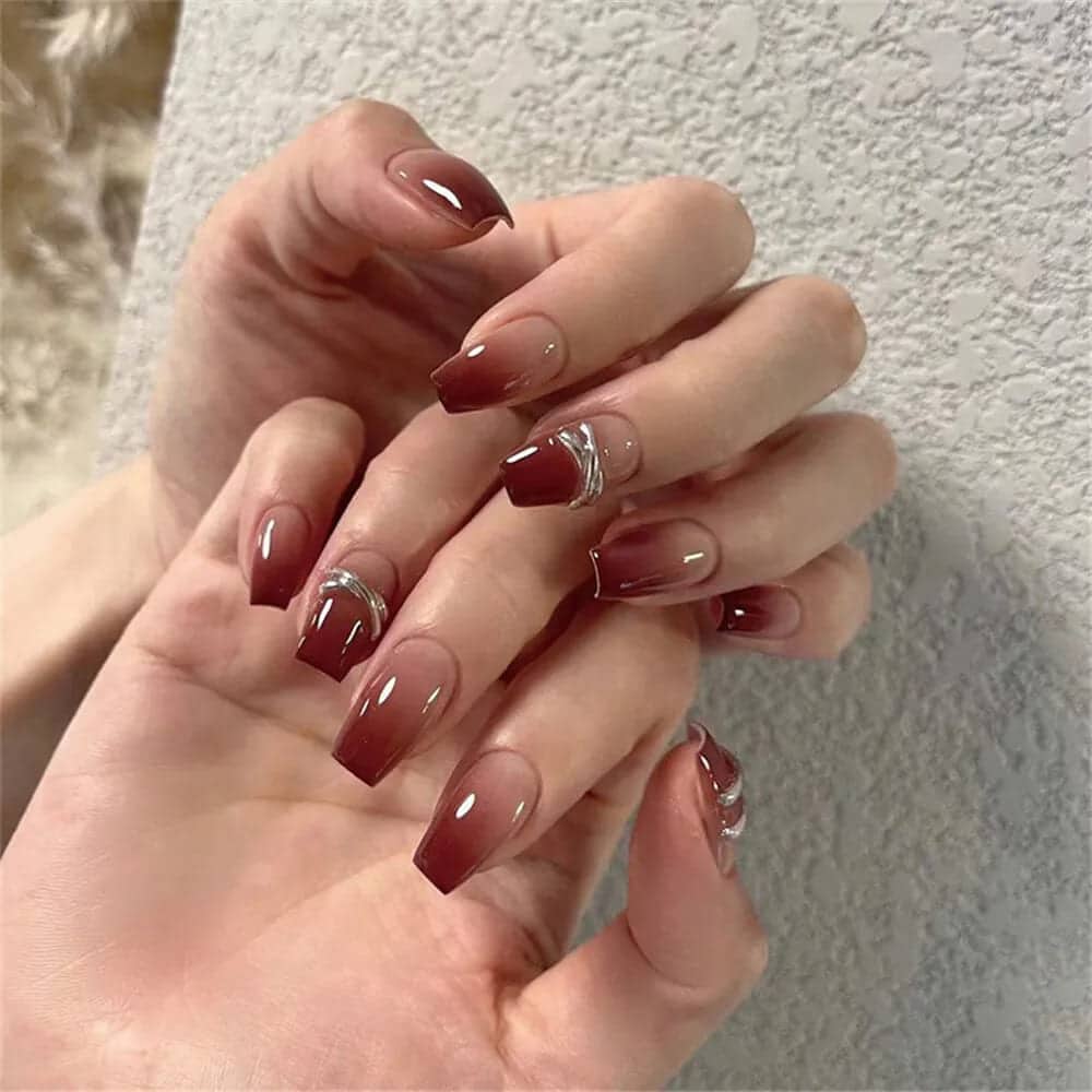 Two hands displaying burgundy ombre nails with gemstones on them