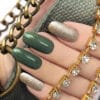 a girls hand along with bag with green and golden nail polish on naisl