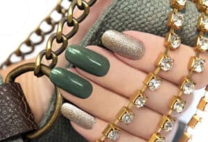 a girls hand along with bag with green and golden nail polish on naisl
