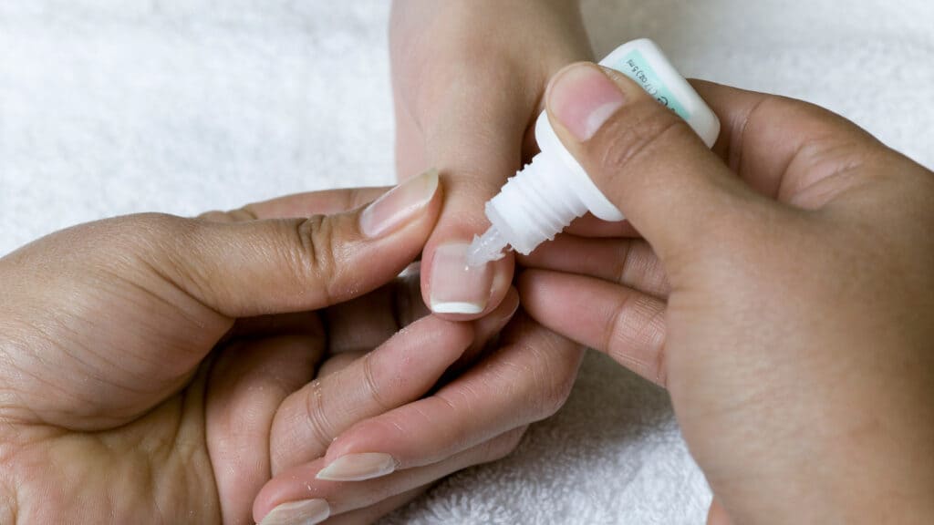 a nail stylist is applying cutical oil on clients nails x