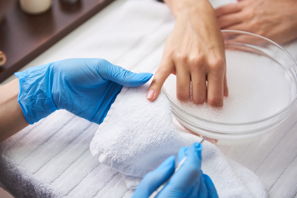 Close up of female arm dipping into glass bowl with foam, water and healing oils.