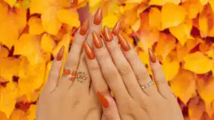 A view of burnt orange nails over autumn leaves