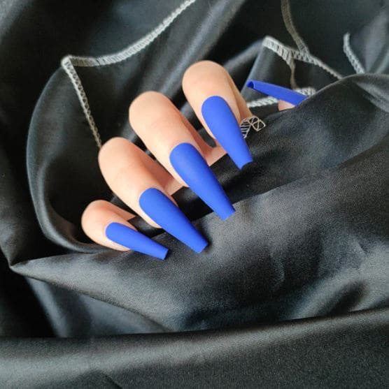 A hand showing off dark blue coffin nails out of a black cloth A hand showing off dark blue coffin nails out of a black cloth