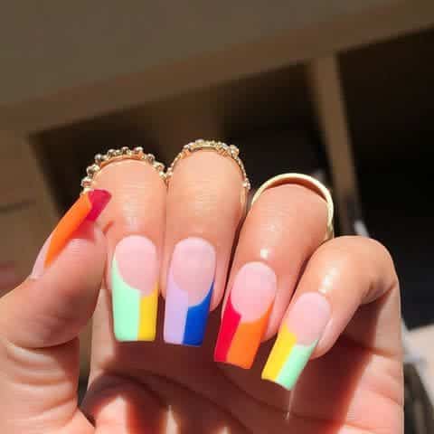 A hand showing off rainbow colored square nails A hand showing off rainbow colored square nails