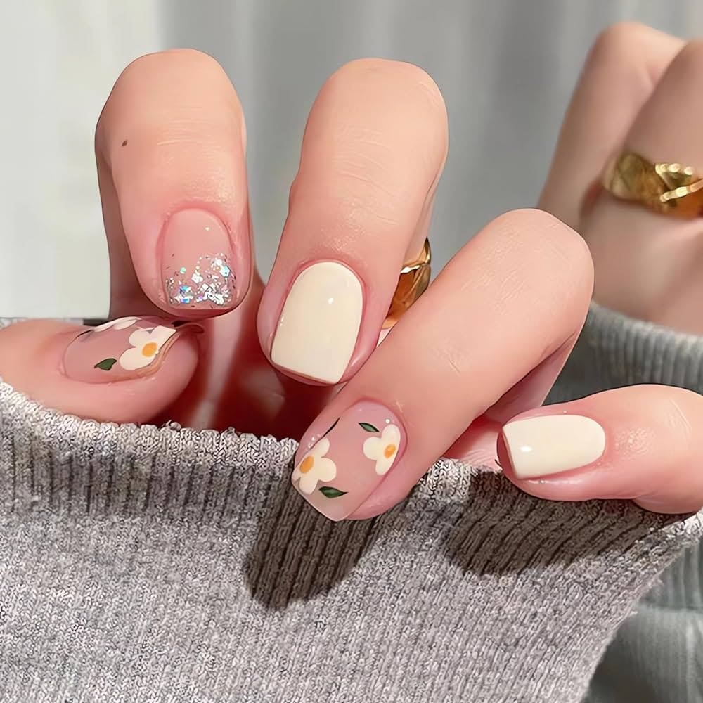 A hand showing off white and nude color on square nails with daisies on them A hand showing off white and nude color on square nails with daisies on them