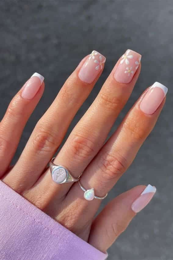 A hand with rings displaying square nails and french white tips with flowers A hand with rings displaying square nails and french white tips with flowers